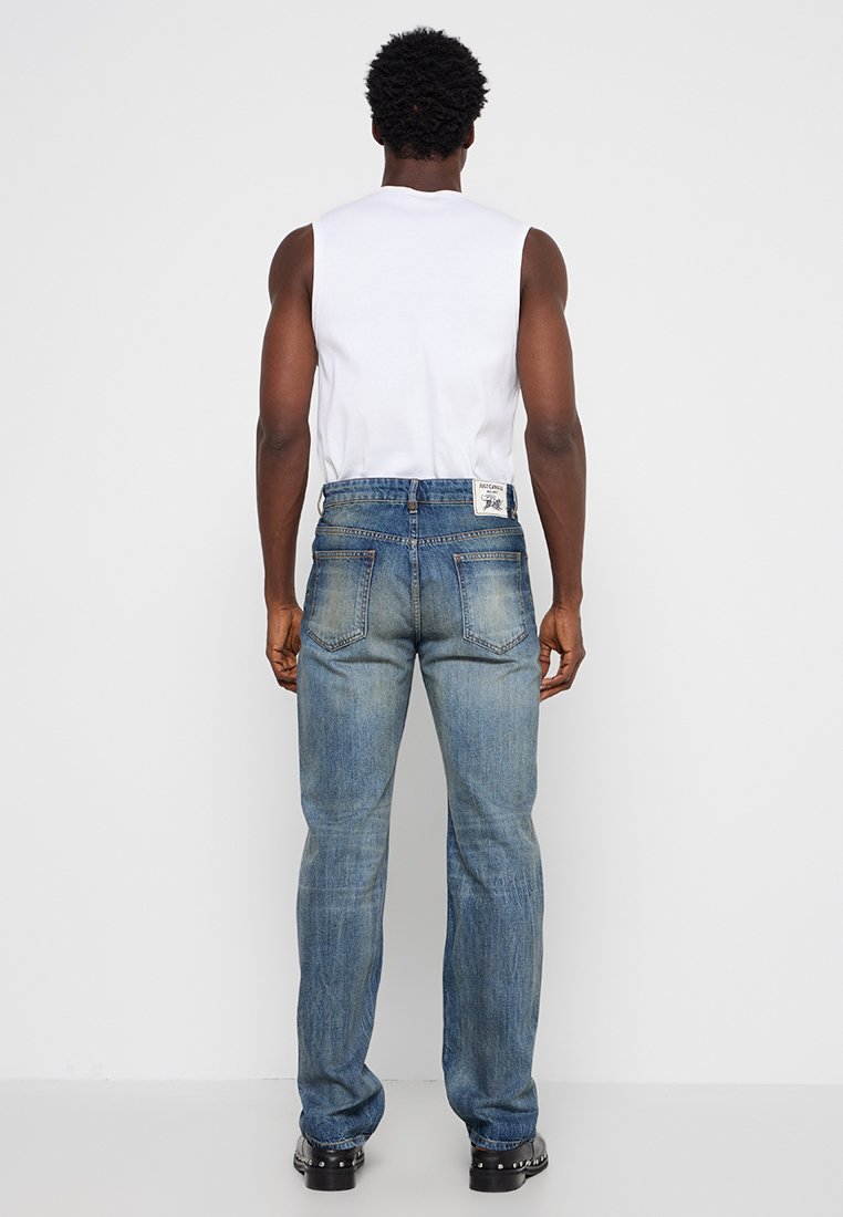 Jean en denim bleu clair avec une coupe droite, arborant une étiquette blanche près de la taille et un léger délavage dans la texture du tissu.