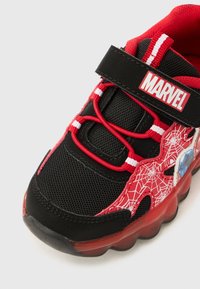 Svart og rød barne-sneaker med Marvel-logo på stroppen, røde webbing-skoelisser, edderkoppnett-design og gjennomsiktig rød såle.