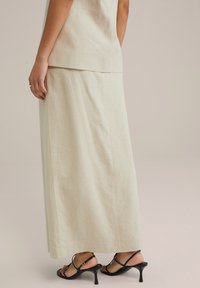 Beige linnen maxi rok met een strak design, gecombineerd met zwarte sandalen met hakken en straps die slanke hielen en een minimalistische uitstraling hebben.