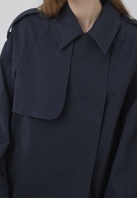 Navy blue coat in cotton blend with a large collar, shoulder epaulets, and side pockets. Features a smooth texture and minimalist design.