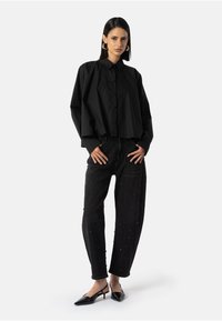 Juodas trumpas mygtukinis marškinėliai su apykakle, derinami su juodomis dekoruotomis džinsais, turinčiais tekstūrinį pynimą. Išvaizdą užbaigia juodi aštrūs bateliai su aukštu kulnu.