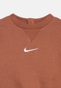 Rjava majica z okroglim izrezom, z rebrastim ovratnikom in belim logotipom Nike Swoosh, postavljenim na sredini spodaj pod izrezom.