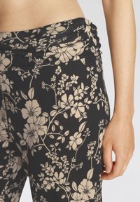 Zwarte leggings met een bloemenpatroon in beige tinten. Voorzien van een brede, geplooide tailleband en een soepele, rekbare stof.