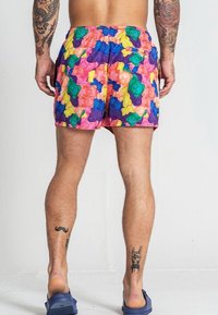 Maillots de bain colorés présentant un motif de oursons en gomme en rose, vert, bleu, jaune et violet, avec une taille élastique et des poches latérales.