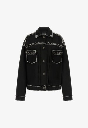 Chaqueta de mezclilla negra con tachuelas plateadas en los hombros, los bolsillos y el dobladillo. Tiene un cuello clásico y cierre de botones al frente.