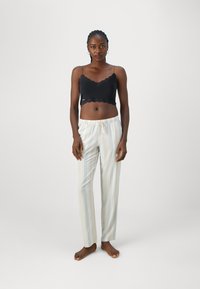 Camisola preta com renda nos bordos e alças finas, combinada com calças de pijama listradas em cores claras, com cintura elástica e cordão.