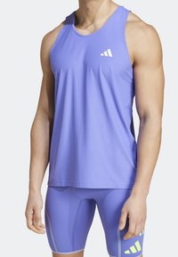 Top da allenamento viola in tessuto testurizzato, con un logo bianco e una vestibilità rilassata. Indossato con pantaloni corti viola abbinati e dettagli grigi.