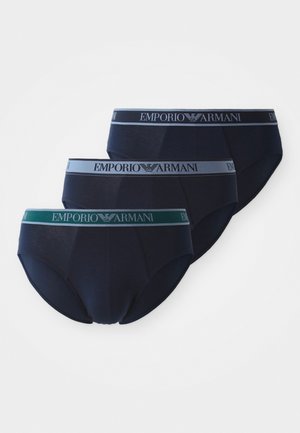 Trois paires de slips bleu marine avec des ceintures élastiques contrastantes. La ceinture du milieu est verte, tandis que les autres sont grises claire et foncée.