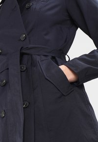 Námořnický trenčkot s opatřeným páskem, dvouřadým zapínáním, velkými knoflíky a bočními kapsami. Vyrobeno z hladké, lehké tkaniny.