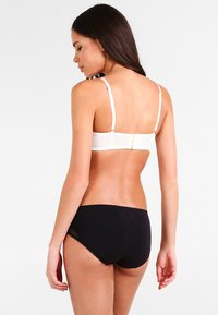 Witte bh met dunne bandjes en een haaksluiting, gecombineerd met zwarte slipjes met kantdetails en een zachte afwerking.