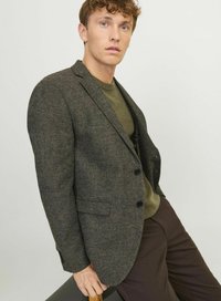 Blazer en chevrons noir en laine texturée avec deux boutons, associé à un pull vert foncé et un pantalon marron. Ventilation simple notable et poches.