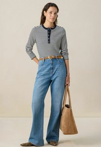 Gestreepte langesleeve top met ronde marineblauwe kraag en knoopsluiting, gecombineerd met high-waisted blauwe jeans en een beige suède handtas.