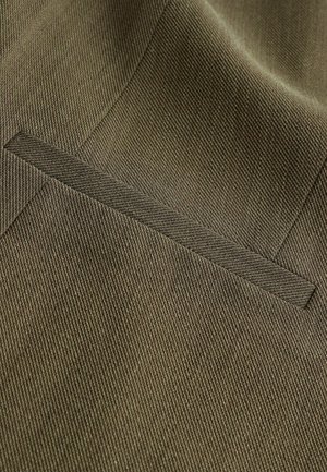 Țesătură de culoare maro, cu o textură subtilă și un model diagonal, având un detaliu de buzunar plat pe o îmbrăcăminte, evidențiind liniile curate și designul minimalist.