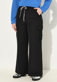 Zwarte cargo-broek met wijde pijpen, een elastische tailleband en grijze trekkoorden, met zijzakken en een gladde textuur.