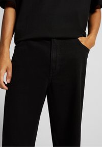 Pantalones negros con una textura suave, que cuentan con bolsillos laterales y un diseño de pierna recta. La tela es resistente y tiene un sutil brillo.