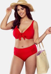 Ensemble de maillot de bain rouge comprenant un top noué et un bas taille haute avec fronces sur les côtés. Un chapeau en paille tressée et un sac fourre-tout léger sont inclus.