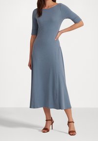 Sininen, polven pituinen mekko kolmannelta neljännekseltä olevilla hihoilla, pyöreällä kaula-aukolla ja pehmeällä tekstuurilla. Yhdistetty ruskeisiin remmikorkkareihin.