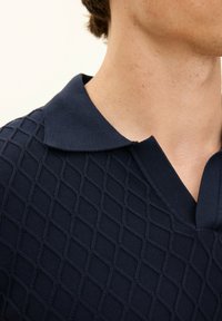 Marinblå polo t-shirt med ett diamantmönstrat stickat mönster, en mjuk krage och V-ringning, vilket framhäver en modern design.