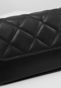 Pochette in pelle nera trapuntata con una superficie liscia, caratterizzata da cuciture a forma di diamante e una forma rettangolare strutturata.