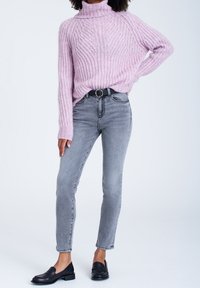 Lila stickad polotröja med ett texturerat mönster, kombinerad med ljusgrå smala jeans och svarta loafers, med ett cirkulärt bälte.