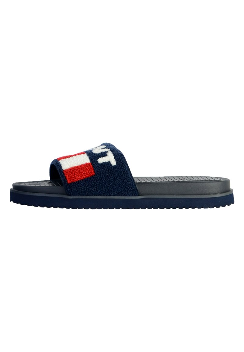 Navy slide sandal featuring a textured, fuzzy strap with a logo and red accents, and a flat rubber sole with a ridged pattern.