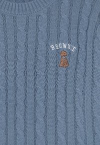 Blaues Kabelstrickgewebe mit einem gestickten kleinen braunen Hund und dem weißen Text "BROWNC" darüber.