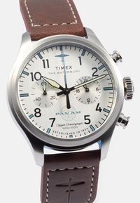 Timex Waterbury horloge met roestvrijstalen kast, witte wijzerplaat, bruine leren band, chronograaf functies, en Pan Am logo.