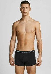 Schwarze Baumwoll-Boxershorts mit einem weißen elastischen Bund, auf dem der Markenname "JACK & JONES" wiederholt ist. Glatte Textur, enganliegendes Design.