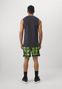 Σκούρο γκρι αμάνικο τοπ, πράσινα σορτς με σχέδιο φίδι και μαύρες �λεπτομέρειες, μαύρες κάλτσες και αθλητικά παπούτσια, απεικονισμένα από πίσω.