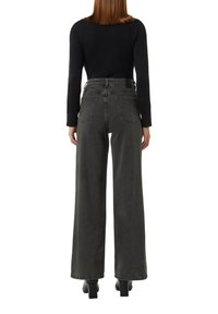 Czarny top z długim rękawem zestawiony z wysoko osadzonymi, szerokimi, ciemnoszarymi jeansami. Posiada szczegółowe przeszycia oraz dwie tylne kieszenie.