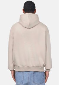 Beige hooded sweatshirt with a relaxed fit, ribbed cuffs, and hem. Soft fabric with a smooth texture, no visible patterns or hardware.