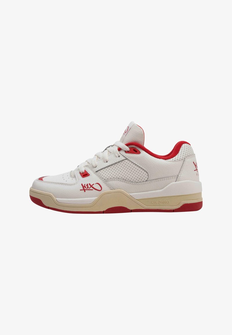 White leather sneaker with red accents, perforated side panels, and a beige midsole. Features laces, logo on the side, and rubber outsole.