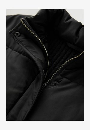 Čierna bunda s vysokým golierom, vybavená predným zipsom, zapínaním na cvoky a textúrovanou vnútornou podšívkou. Hladká, vodeodolná tkanina.