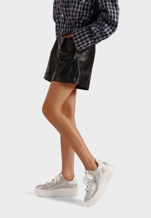 Scarpe da ginnastica argento con suola bianca spessa, superficie testurizzata e lacci bianchi. Indossate con una gonna in pelle nera e una camicia a quadri abbottonata.