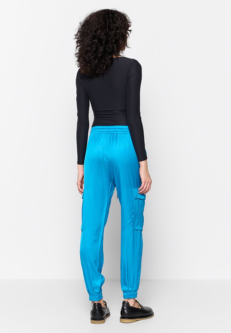 Pantalon de jogging en satin bleu avec taille élastique et poignets à la cheville, doté de poches latérales et d'une texture lisse et brillante. Haut à manches longues noir.