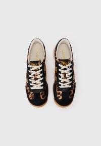 Paire de baskets à motif léopard avec des accents en daim noir, des lacets blancs et des semelles en caoutchouc beige sur un fond blanc uni.