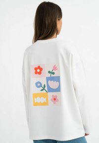 Weißer Pullover mit einem bunten Grafikeindruck auf der Rückseite, unterteilt in sechs Quadrate mit floralen und abstrakten Motiven.