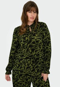 Zelený a černý vzorovaný top s výstřihem ve tvaru klíčové dírky, plisovanou texturou a dlouhými rukávy. Koordinující kalhoty mají stejný design.