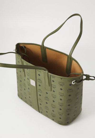 Green MCM tote bag with black logo print, double shoulder straps, and a tan interior, shown open on a white surface.