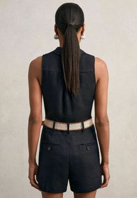 Fekete lenvászon, ujjatlan jumpsuit hátsó zsebekkel, a dérrel bővített derékkal, amelyhez krém- és barna árnyalatú texturált, szőtt öv tartozik.
