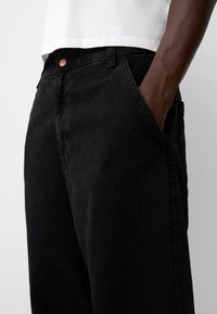 Black denim pants with a loose fit, side pockets, and a button closure. The fabric has a slightly textured finish.