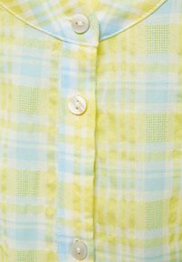 Camicia leggera a quadri in giallo pastello e blu, con un'apertura a bottoni frontale dotata di bottoni bianchi e un colletto morbido.