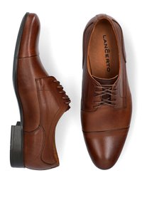 Brązowe skórzane buty do garnituru z gładką teksturą, okrągłym noskiem, dekoracyjnym przeszyciem i niskim obcasem z kontrastującą czarną podeszwą.