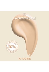 Échantillon de crème beige avec une texture lisse et brillante, étiqueté "10 Ivoire." Un emblème circulaire blanc met en avant "97 % d'ingrédients naturels."