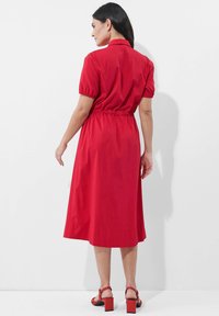 Rotes, kurzärmeliges Kleid mit taillierter Passform und fließendem Rock. Verfügt über einen Kragen und eine elastische Raffung im Rücken. Glatte Stofftextur.