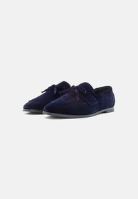 Loafers din catifea albastră navy, cu un design elegant, având un accent sub formă de fundiță și o talpă plată din cauciuc. Textura este moale, cu un finisaj neted.