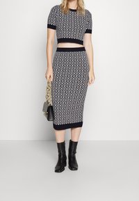 Dwuczęściowy zestaw dzianinowy składający się z krótkiego topu i spódnicy midi, w kolorze granatowym z białym geometrycznym wzorem, zestawiony z czarnymi botkami za kostkę i torebką na łańcuszku.