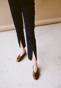 Pantaloni in denim scuro con spacchi laterali, abbinati a scarpe slip-on in pelle marrone. Focus sulla texture del tessuto e sul design pulito e minimalista.