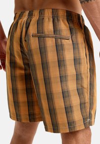 Shorts a cuadros naranjas y negros con cinturilla elástica, que cuentan con un bolsillo trasero y un patrón de tela tejida texturizada.