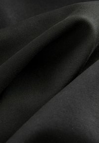 Detailní záběr na překrývající se černou látku, ukazující texturu a záhyby, zdůrazňující její hladkost a hustotu.